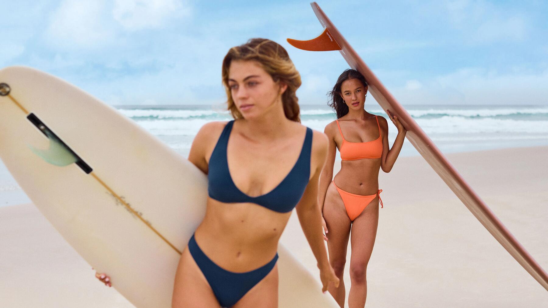 Twee vrouwen op het strand met een surfboard en sportbikini's aan
