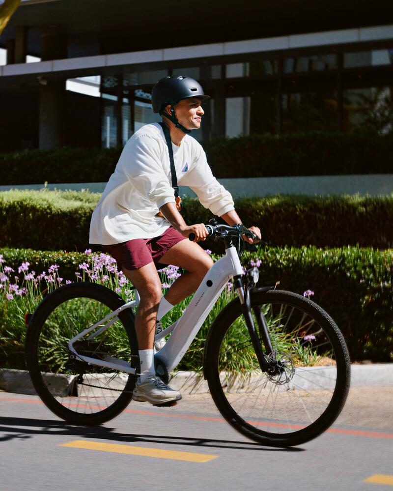Muškarac sa kacigom vozi beli električni bicikl.