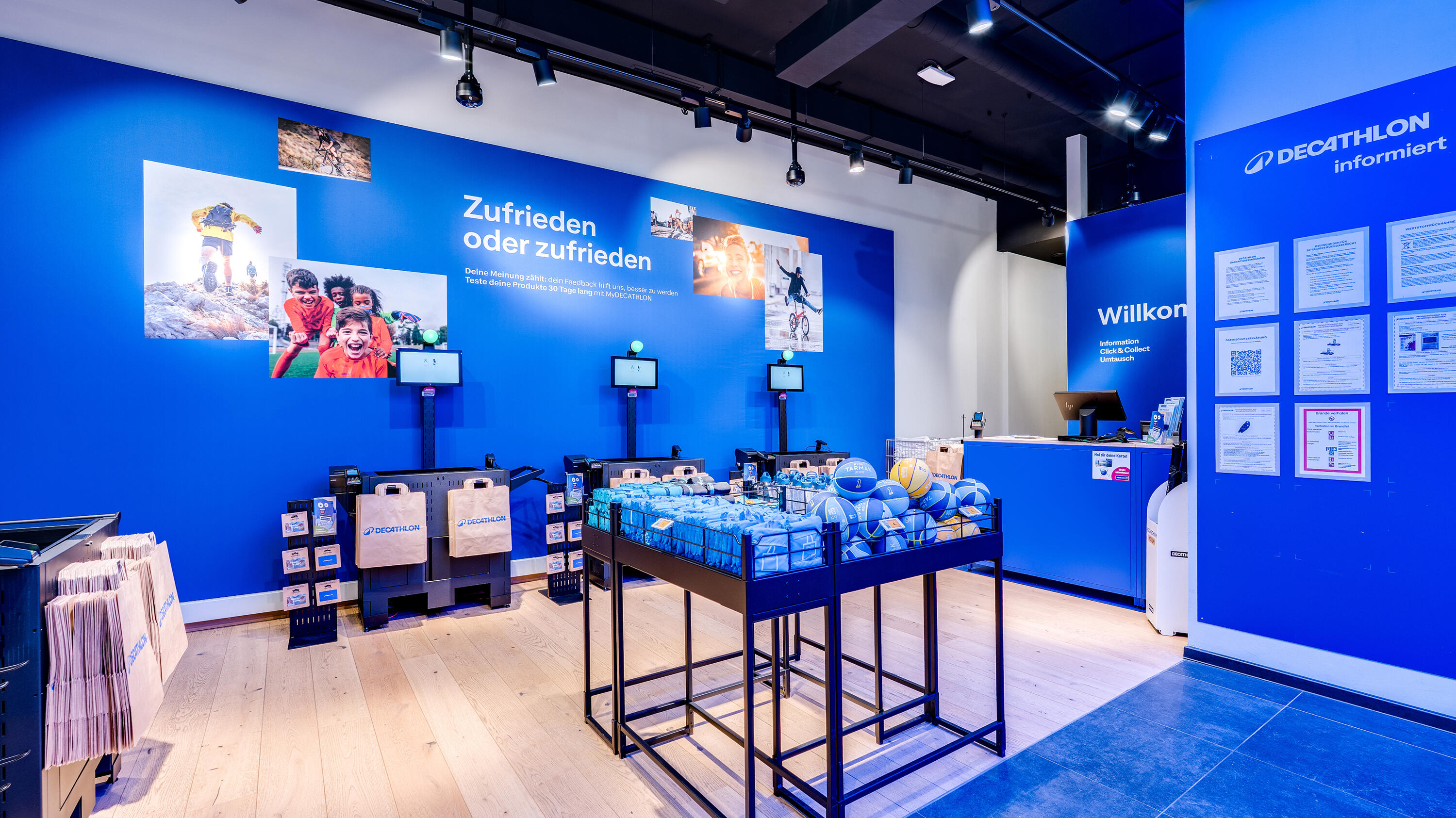 Servicebereich und Kassen einer Decathlon-Filiale mit blauen Wänden, Sportfotos und Self-Checkout-Terminals.
