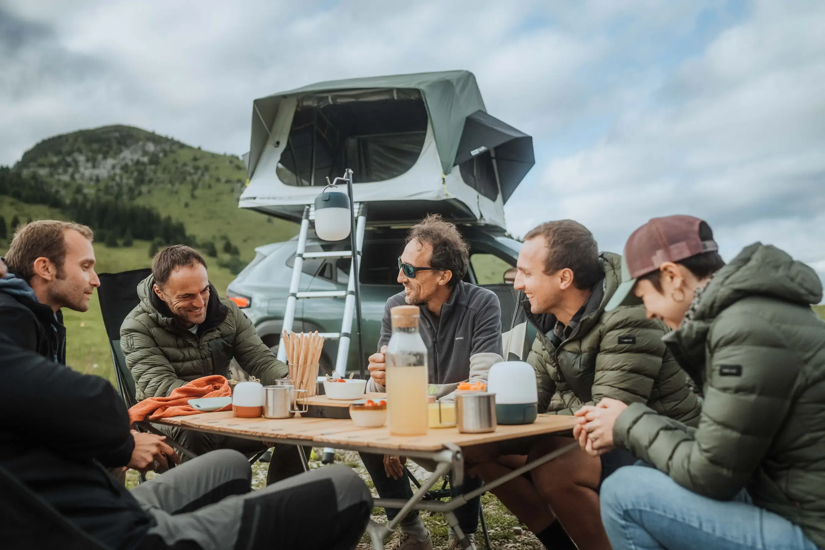 Vanlife: Menschen campen und sitzen am Tisch vor einem Auto mit Dachzelt