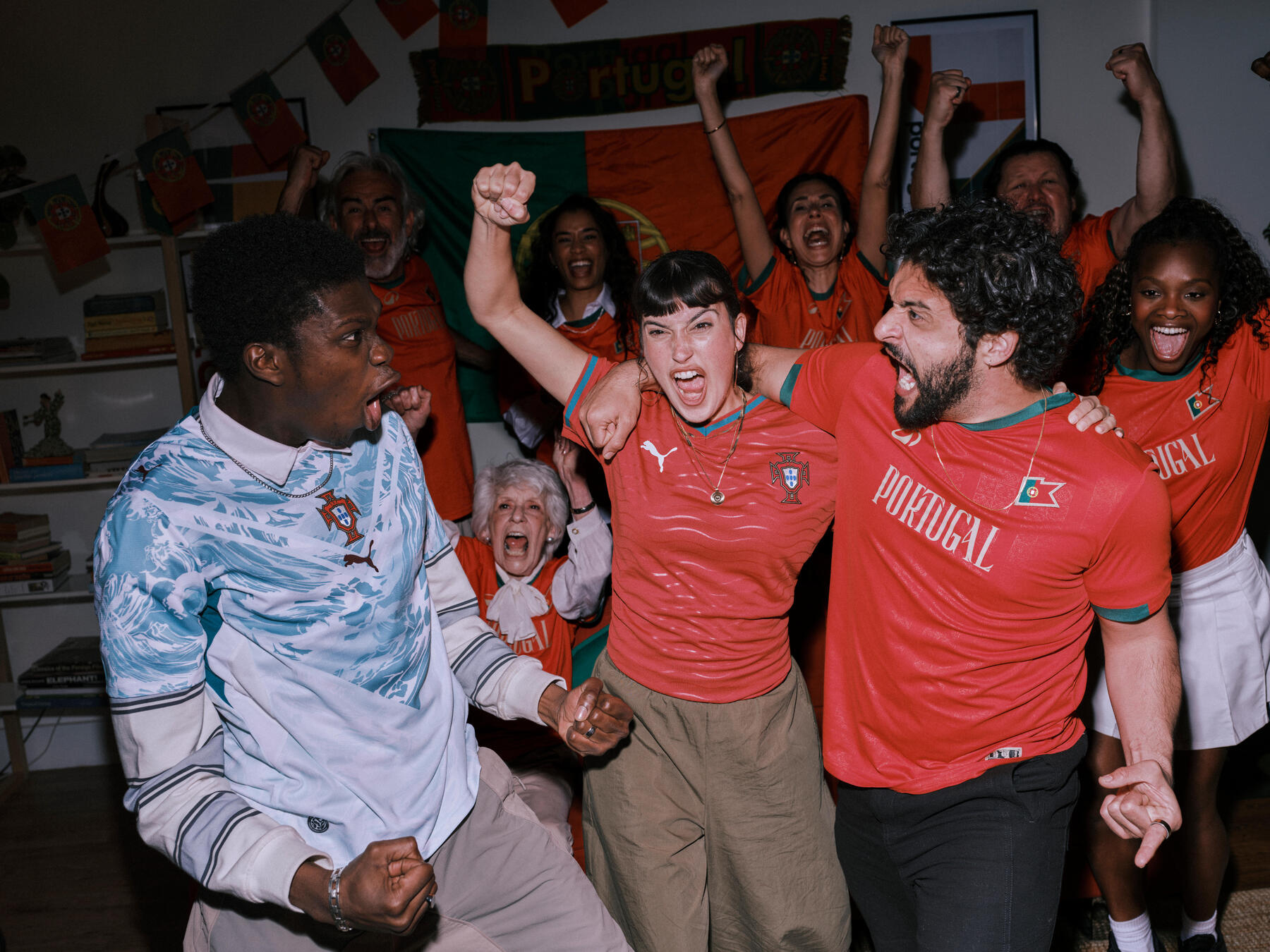 Eine diverse Gruppe begeisterter Fans jubelt euphorisch in Portugal-Trikots vor einer passenden Landesflagge und Dekoration.
