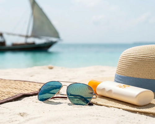 Okulary przeciwsłoneczne krem spf i kapelusz leżące na plaży