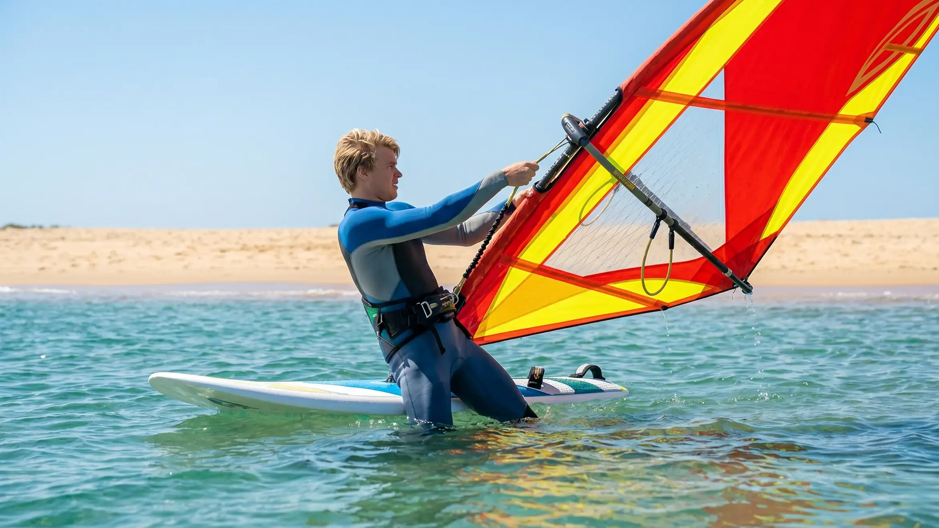 Mężczyzna w wodzie z deską i żaglem do windsurfingu