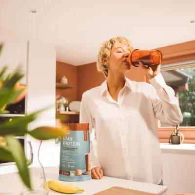Eine Frau trinkt in der Küche einen gesunden Proteinshake