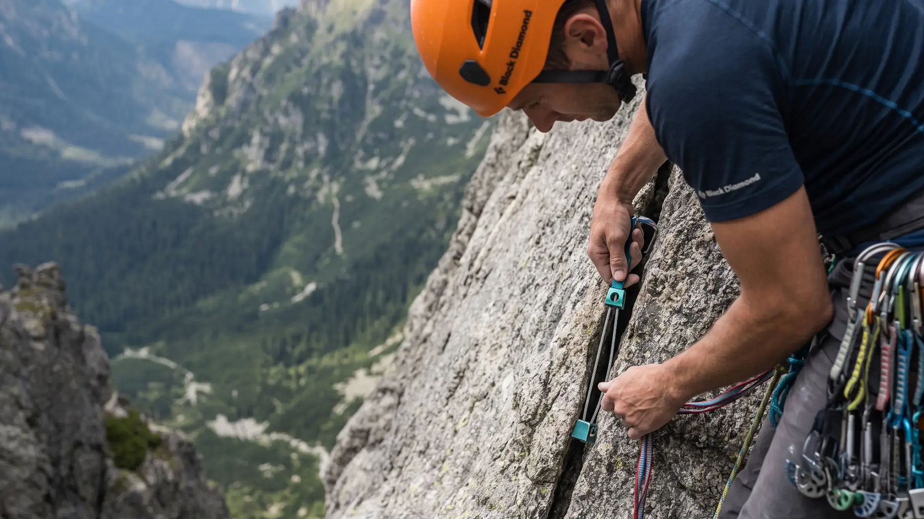 Alpinista w kasku montujący kości wspinaczkowe w skale