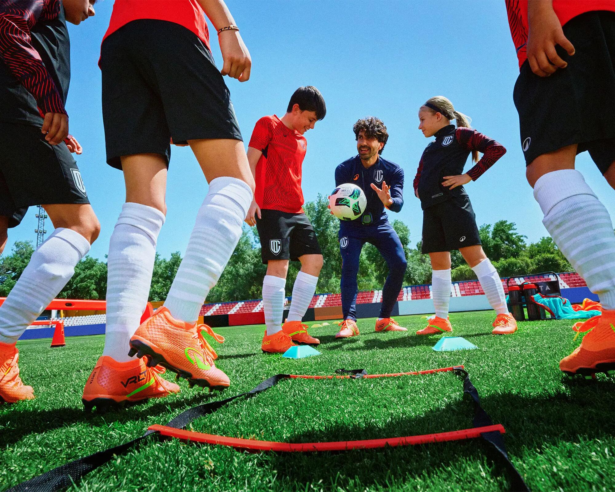 Fußballtrainer erklärt Kindern beim Vereinstraining auf dem Rasenplatz eine Übung mit dem Ball
