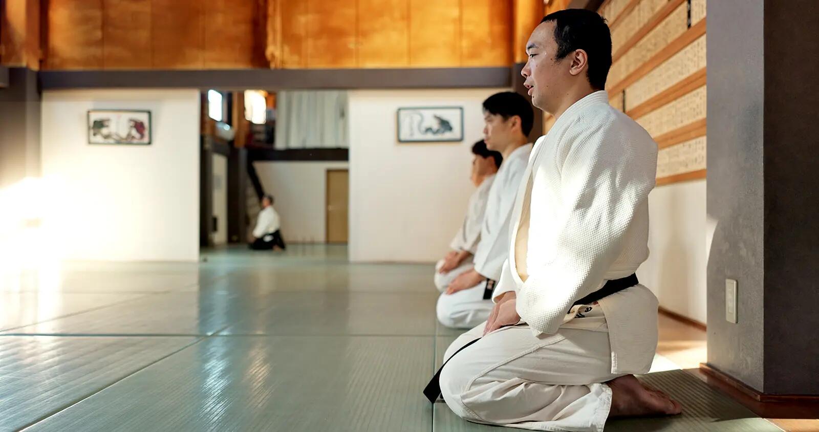 Mężczyźni w strojach do karate siedzący na kolanach na sali