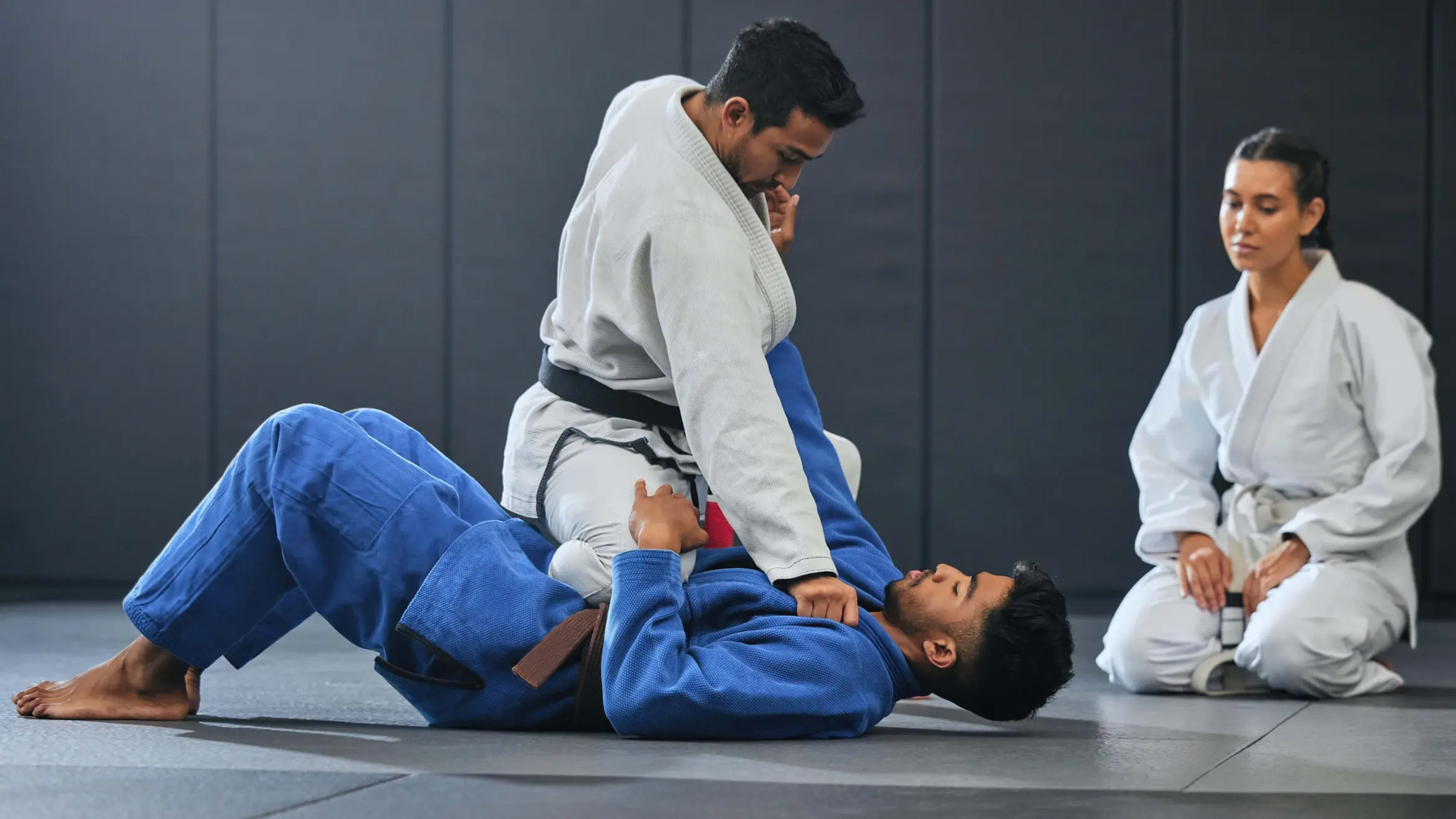 Mężczyźni trenujący karate na macie obok kobieta