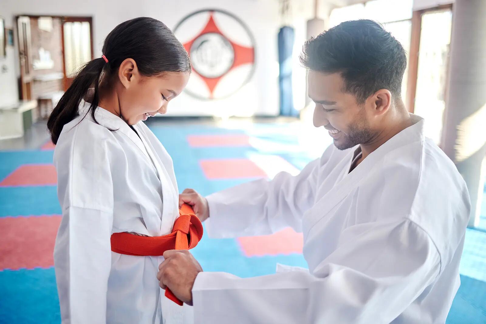 Nauczyciel karate zawiązujący karatege pasem dziewczynce