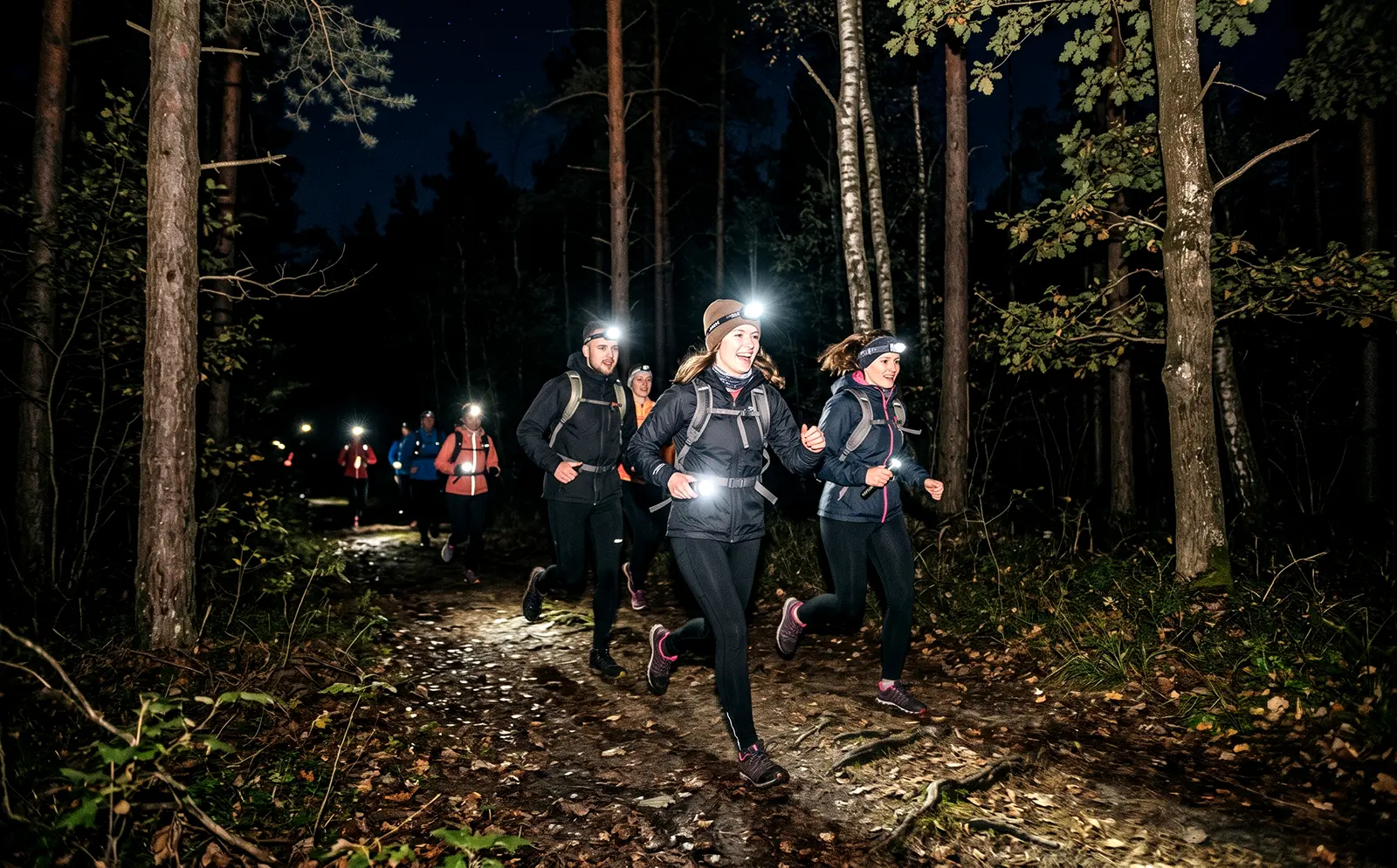 Młodzież w czołówkach biegająca po lesie biorąca udział w nocnej grze terenowej