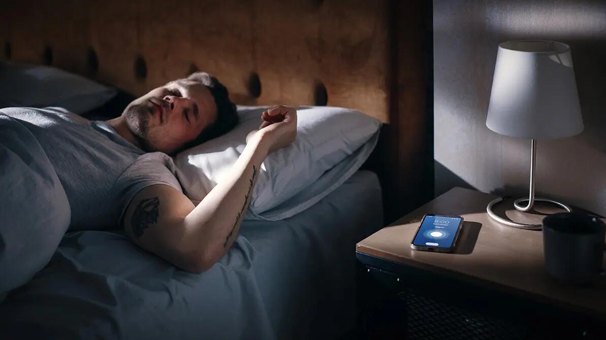 Śpiący mężczyzna obok na szafce nocnej dzwoniący budzik w telefonie