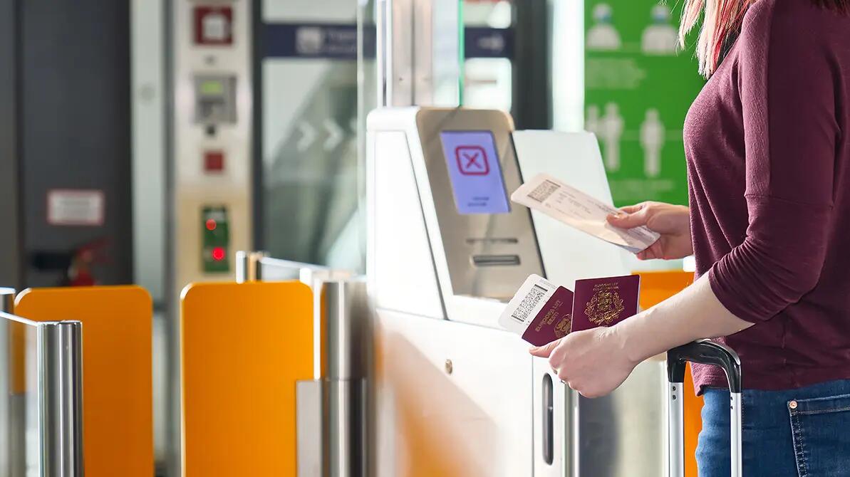 Kobieta stojąca przed bramką biometryczną z kartą pokładową w ręku