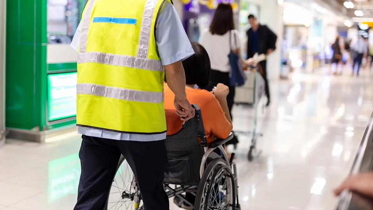 Asystent lotniska prowadzący osobę na wózku po terminalu
