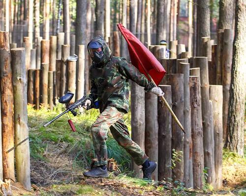 Mężczyzna biegajacy z pistoletem od paintballa i flagą w ręku grający w grę zdobywanie flagi
