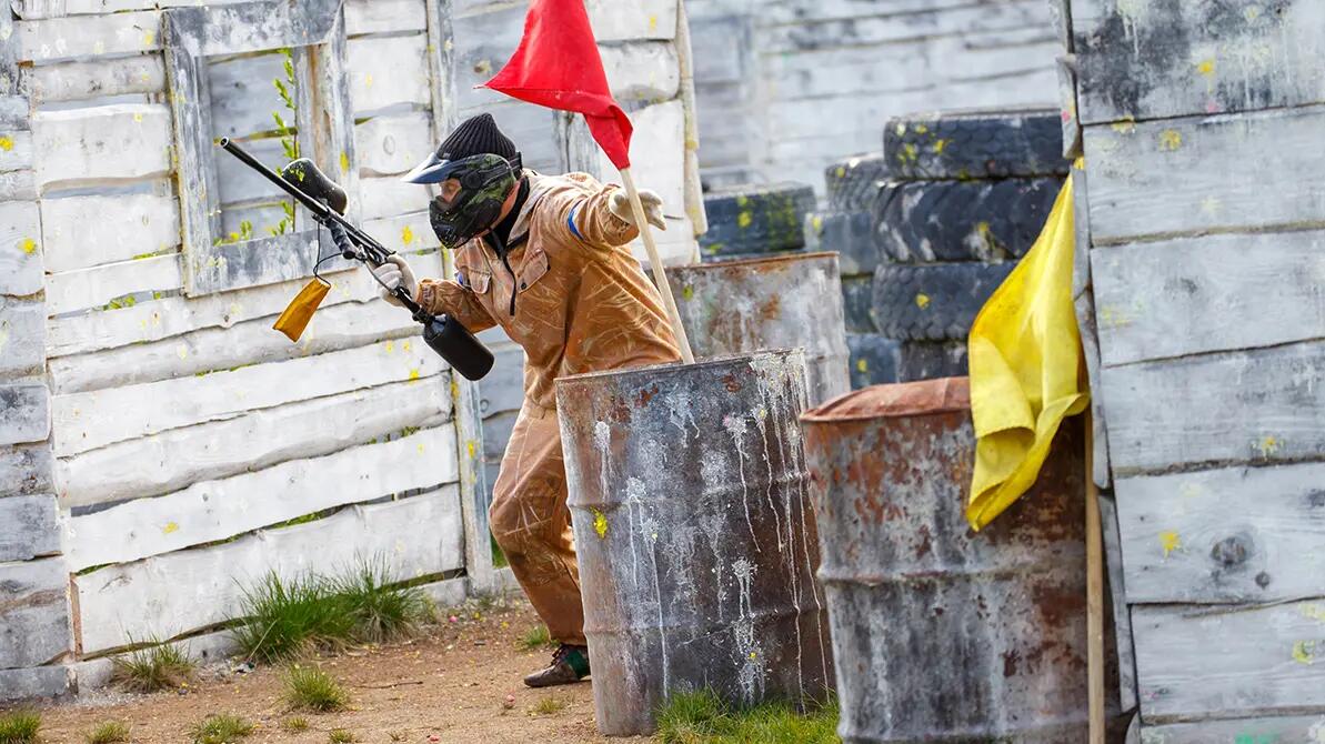 Mężczyzna biegajacy z pistoletem od paintballa i flagą w ręku 