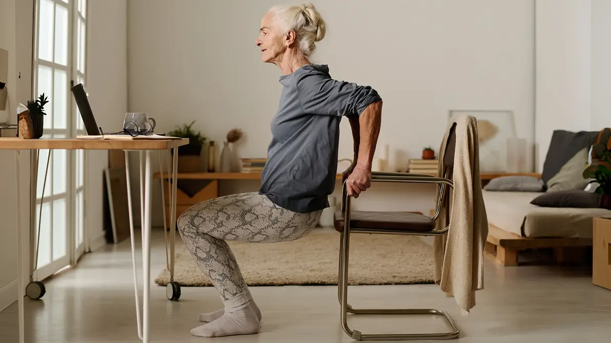Seniorka ćwicząca z krzesłem przysiady