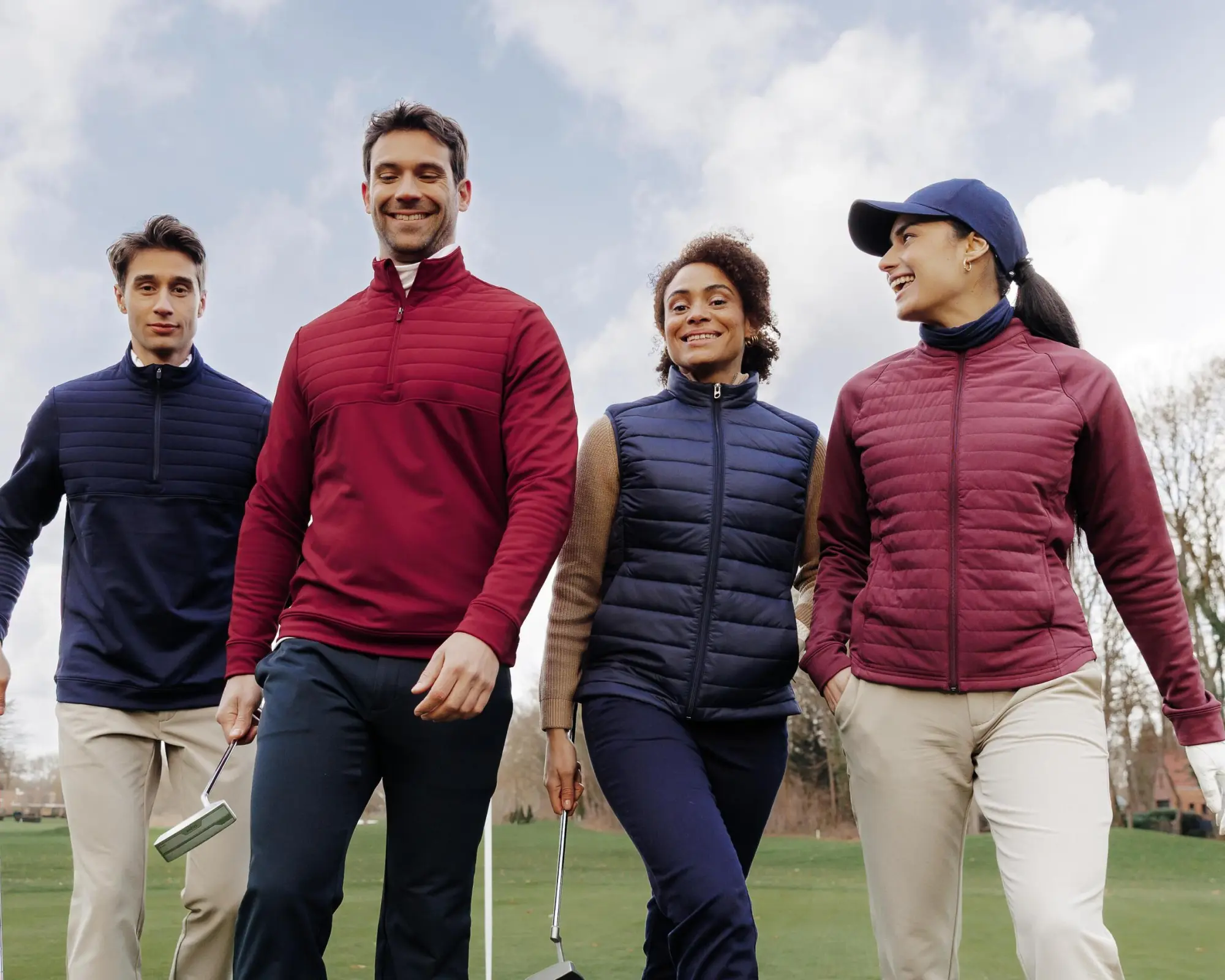 zwei Männer und zwei Frauen stehen auf dem Golfplatz mit herbstliche Golfoutfits