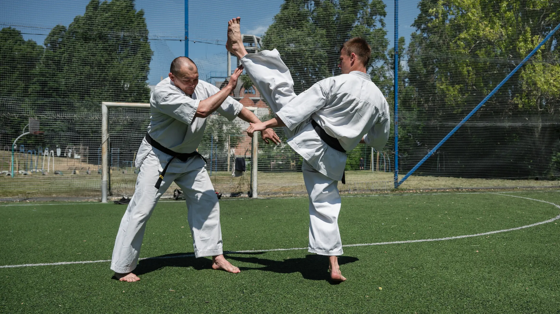 Dwóch mężczyzn w karategach trenujący axe kick na murawie