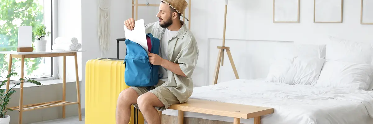 Mężczyzna siedzący na ławeczce w pokoju chowający laptop do plecaka