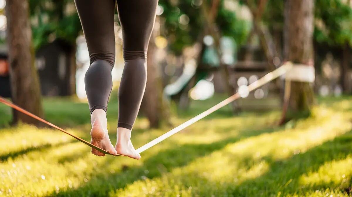 Kobieta idąca po slackline założonej między drzewami