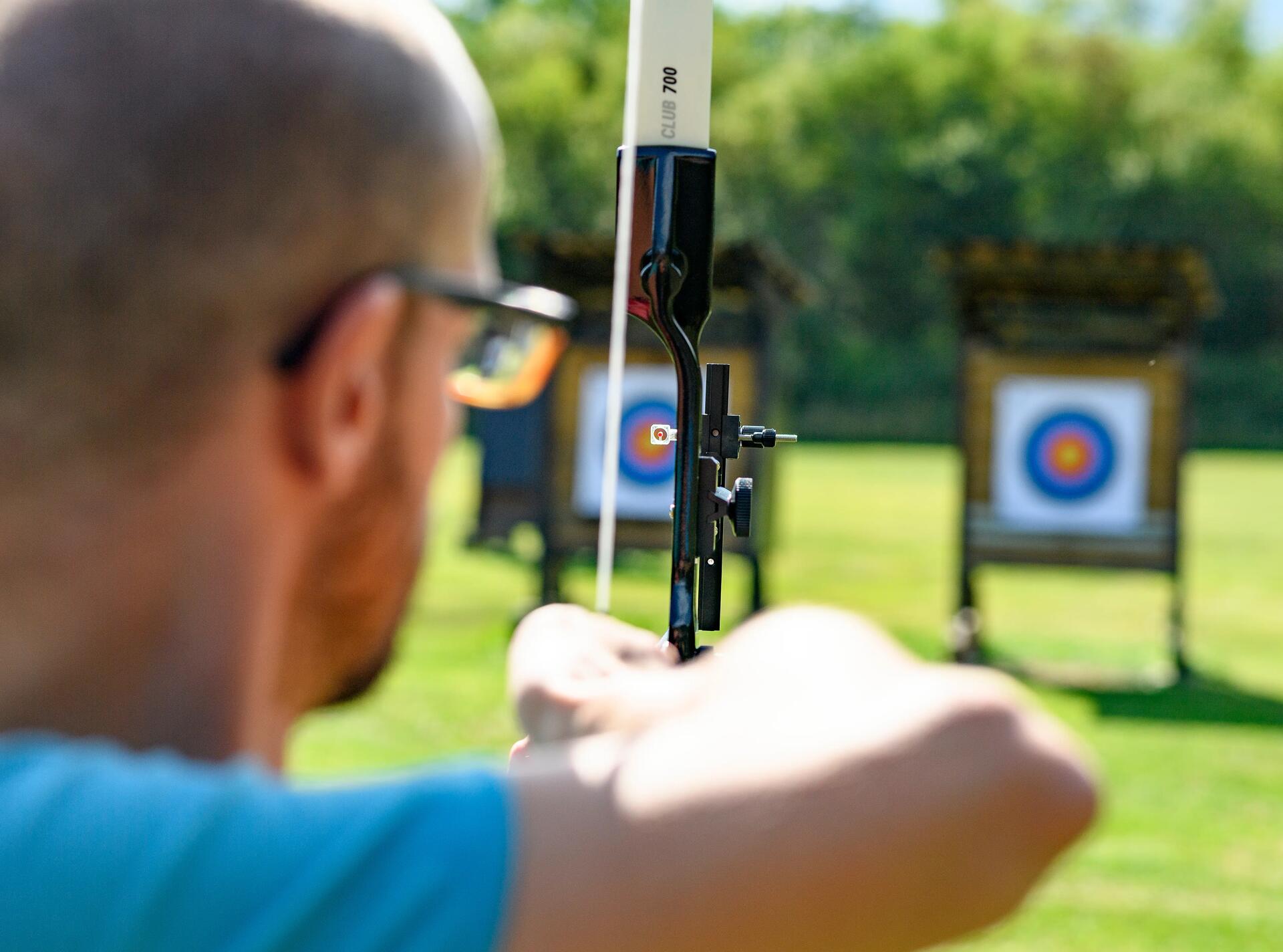 man holding and aiming an archery bow and arrow  at a target