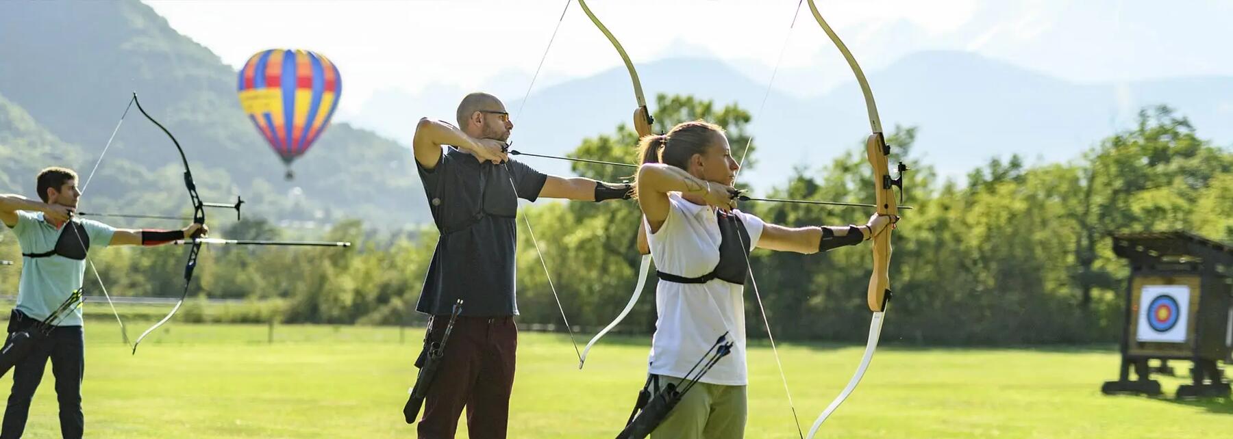 A woman and two men pointing their archery bows and arrows