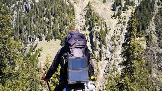 mężczyzna stojący przed górą z kijkami trekkingowymi i plecakiem turystycznym na plecach