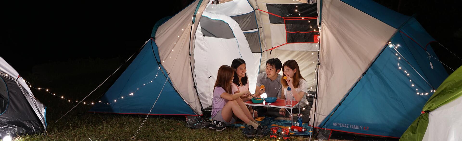rodzina siedząca wieczorem w namiocie przy stoliku turystycznym