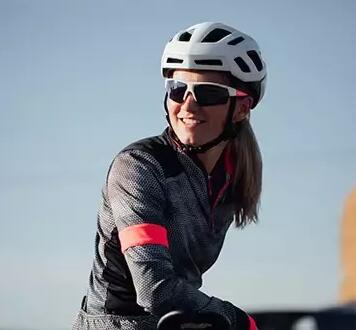 A woman smiling wearing a cycling helmet and cycling glasses.