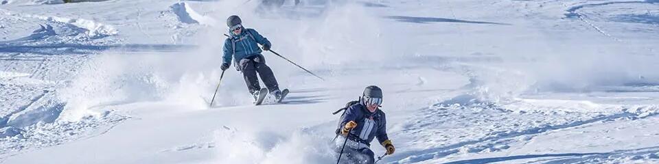 mężczyźni w strojach narciarskich i kaskach zjeżdżający ze stoku na nartach