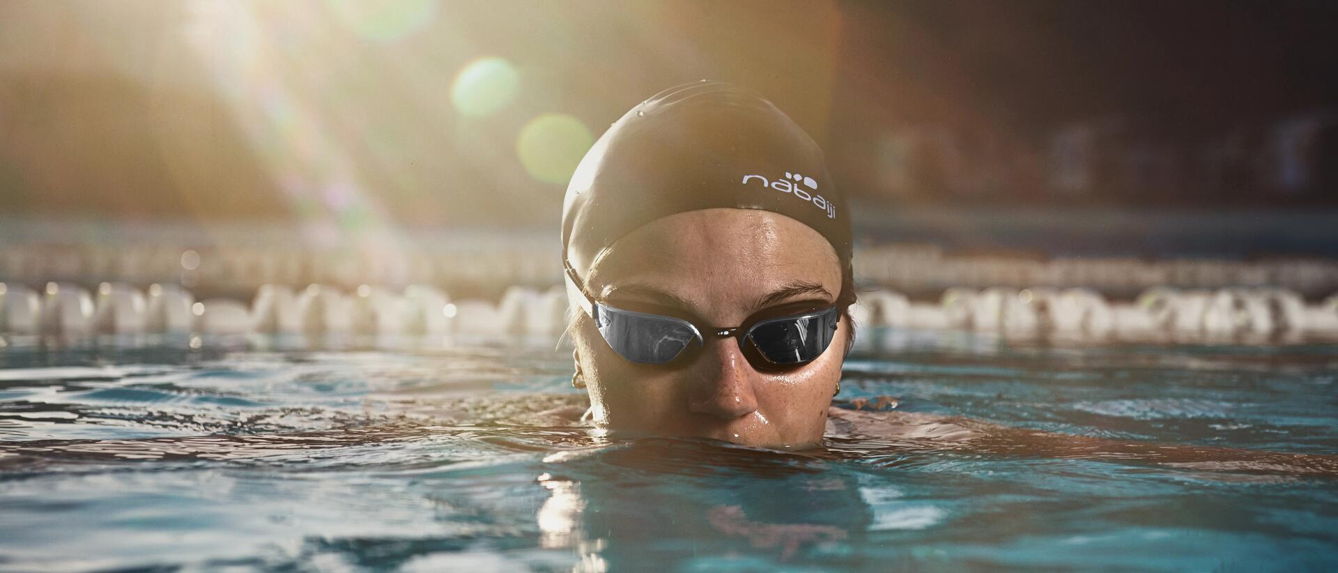 osoba w czepku i okularach pływackich zanurzona w wodzie na basenie