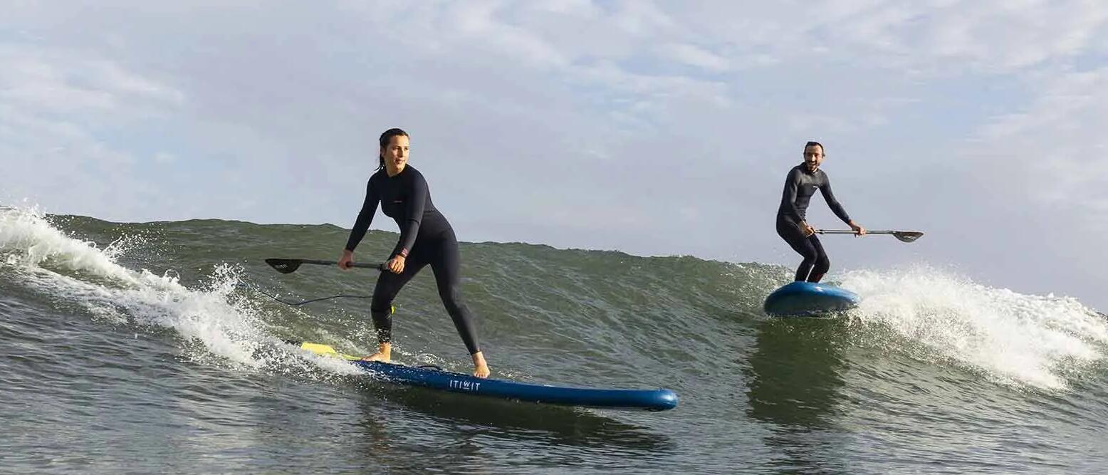A couple surfing a wave on a stand up paddle board.