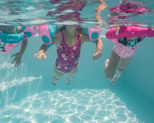 dzieci pływające w strojach kąpielowych z kołami i rękawkami do pływania