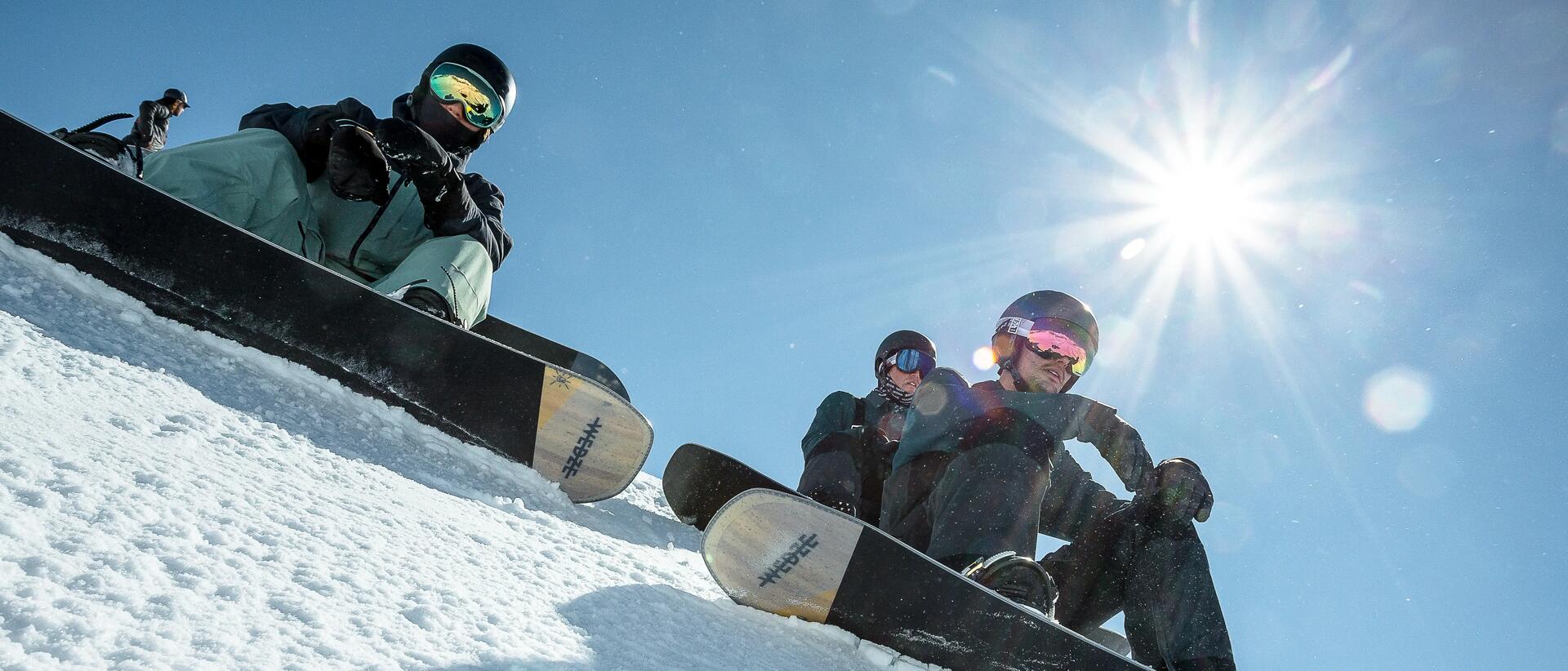 mężczyźni siedzący na śniegu z deskami snowboardowymi