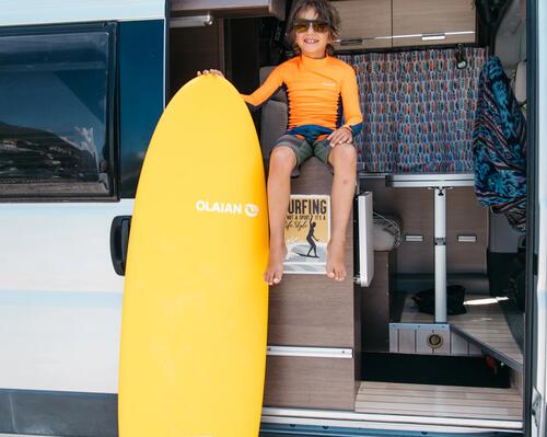 chłopiec w stroju pływackim trzymający deskę surfingową w kamperze