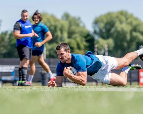 Man clutching rugby ball as he lands on the ground. 