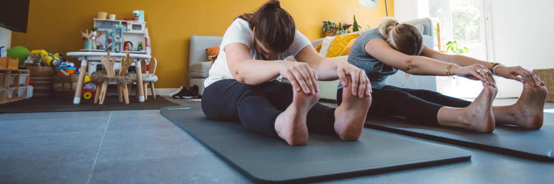 Kobiety w odzieży sporotwej siedzące na macie trzymające ręce na palcach u stóp