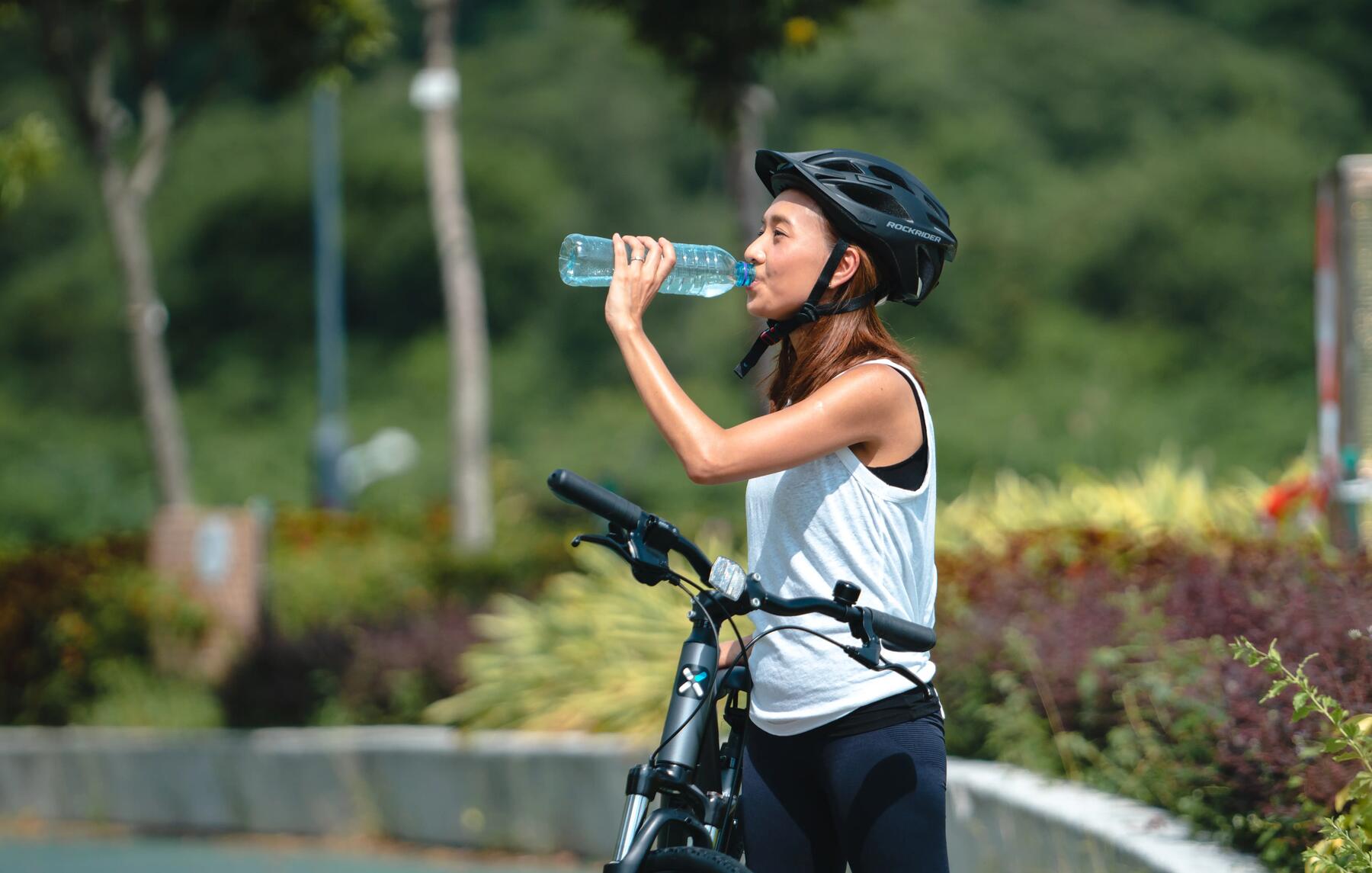 kobieta w odzieży sportowej i kasku pije wodę na rowerze