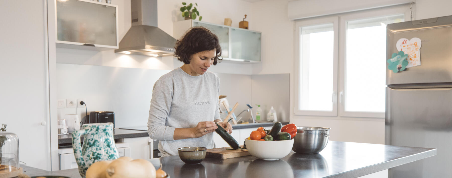 En kvinna står i sitt kök och skalar en gurka