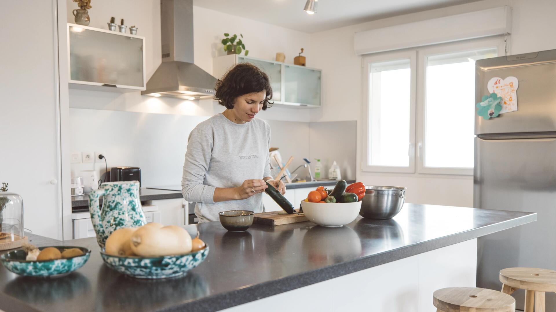 En kvinna står i sitt kök och skalar en gurka