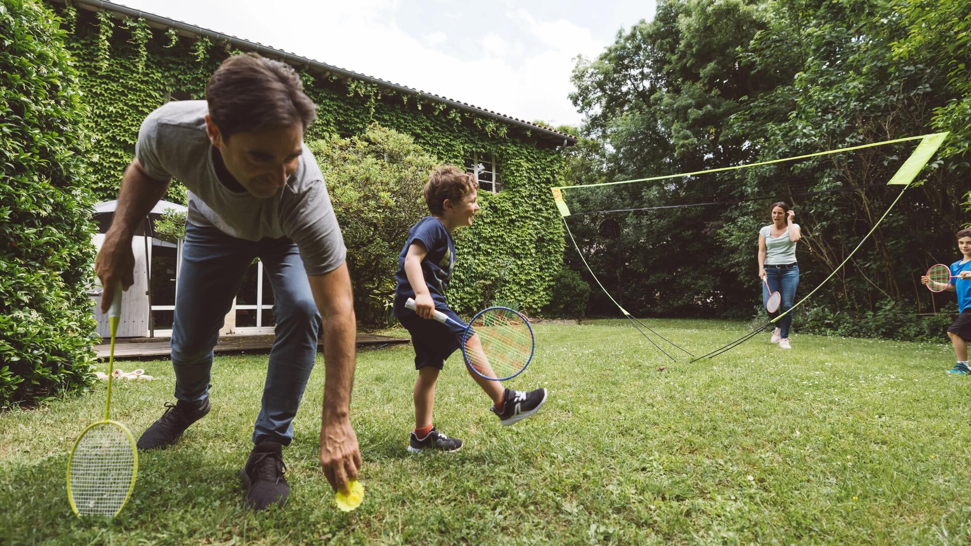 mężczyzna w butach do badmintona podnoszący lotkę badmintonową podczas gry z rodziną 