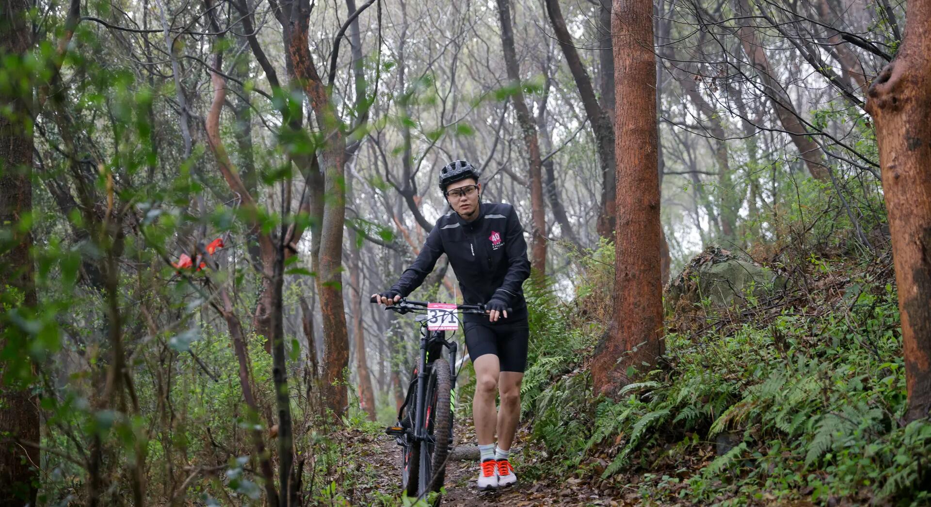 mężczyzna w odzieży rowerowej i kasku prowadzący rower przez las