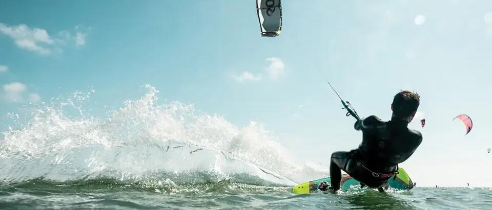 mężczyzna w piance pływackiej pływający na desce kitesurfingowej