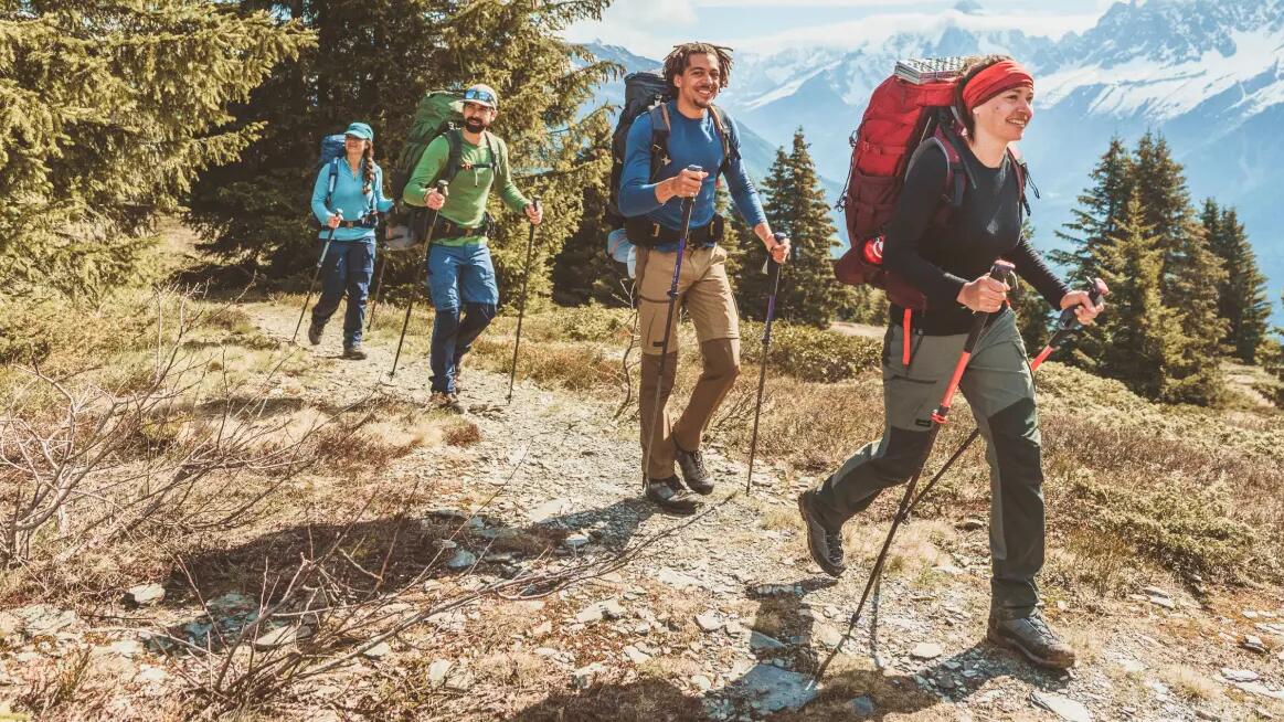 ludzie wędrujący po górach w odzieży trekkingowej z plecakami turystycznymi na plecach i kijami trekkingowymi w rękach