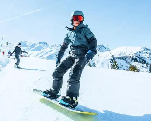 chłopiec w kasku i goglach snowboardowych zjeżdżający na desce snowboardowej ze stoku
