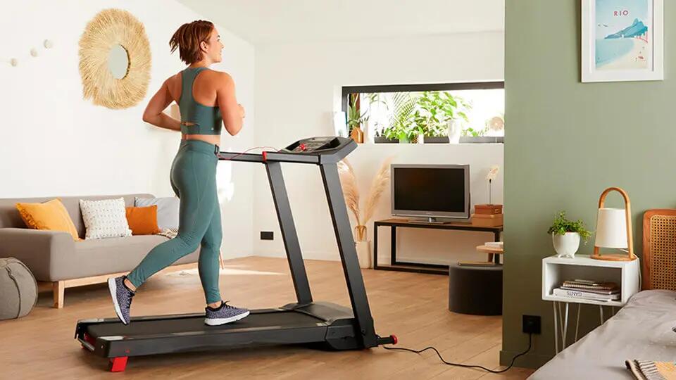 une femme qui s'entraine sur son tapis de course dans son appartement