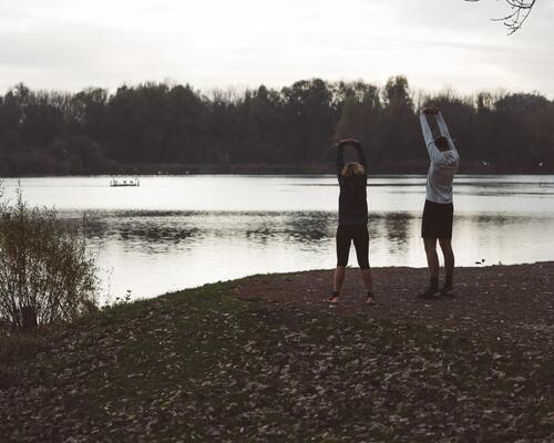 Två människor står invid en sjö och stretchar