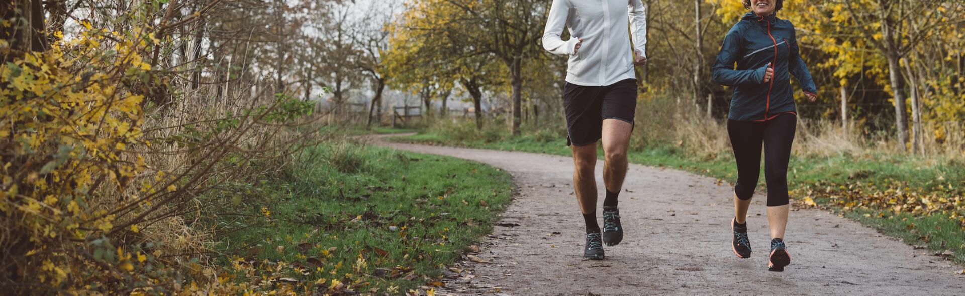 Two people running through forest on path.