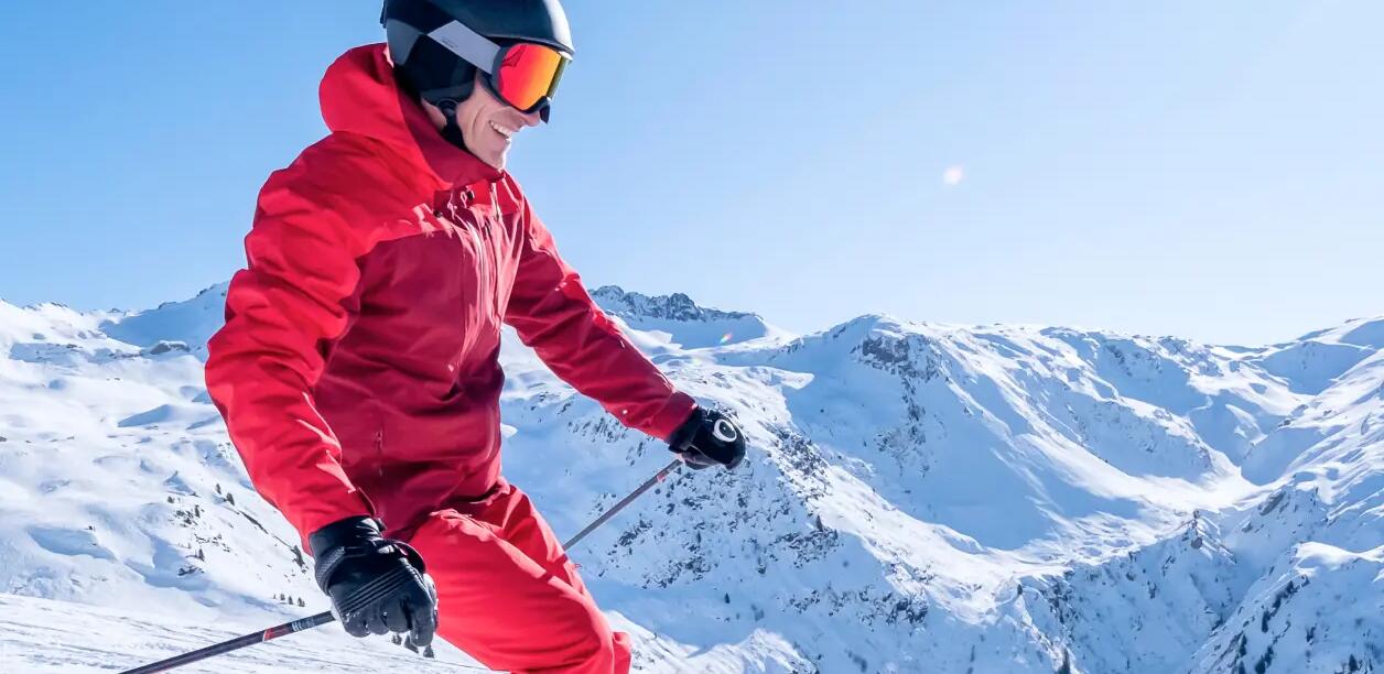 mężczyzna w kasku i odzieży narciarskiej zjeżdżający ze stoku na nartach
