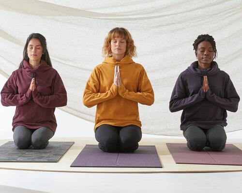 three ladies kneeling on yoga mats with their eyes closed  and palms in prayer pose.